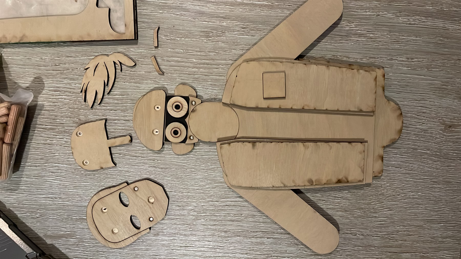 Laser-cut plywood character prototype with loose face and hair components laid out on a work surface